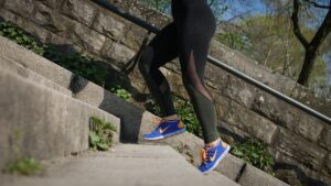 Une femme en jogging gris et baskets montant des marches en courant, illustrant le sport pour perdre du poids.