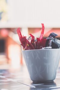 Une tasse en céramique entourée de sachets de sucre blanc et de petits sachets d’édulcorants, illustrant la thématique des alternatives au sucre.